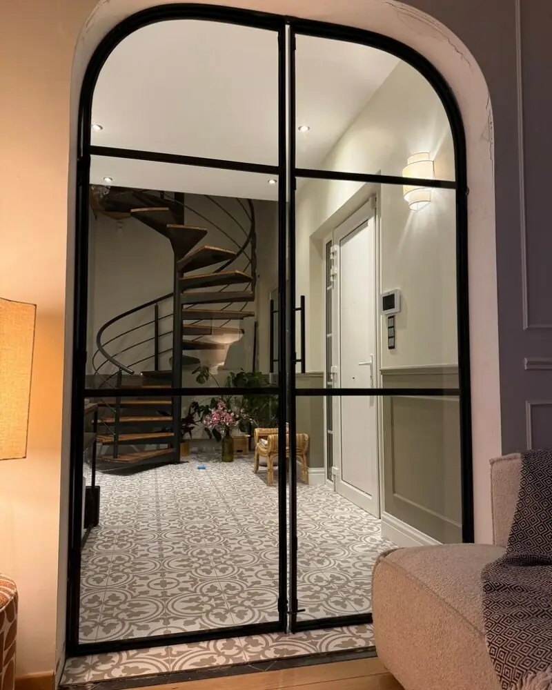 Porte cintrée en acier et verre donnant sur un escalier en colimaçon